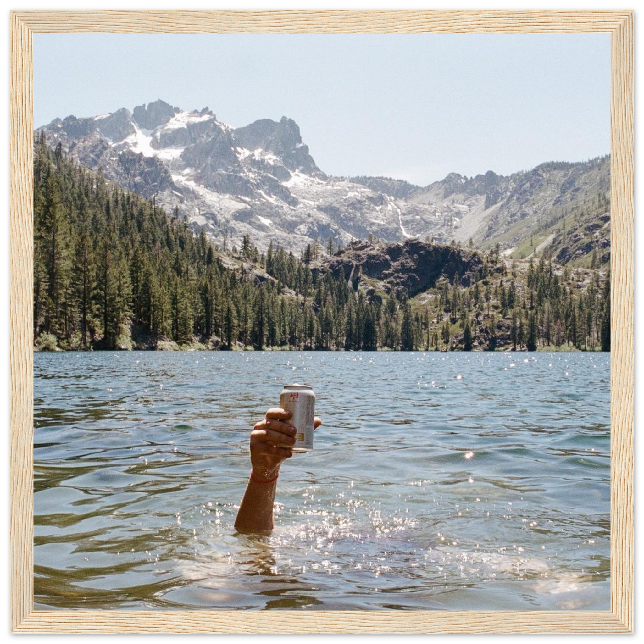 Adventure photography print of hand holding beer in alpine lake with mountains and trees, lifestyle wall art, framed