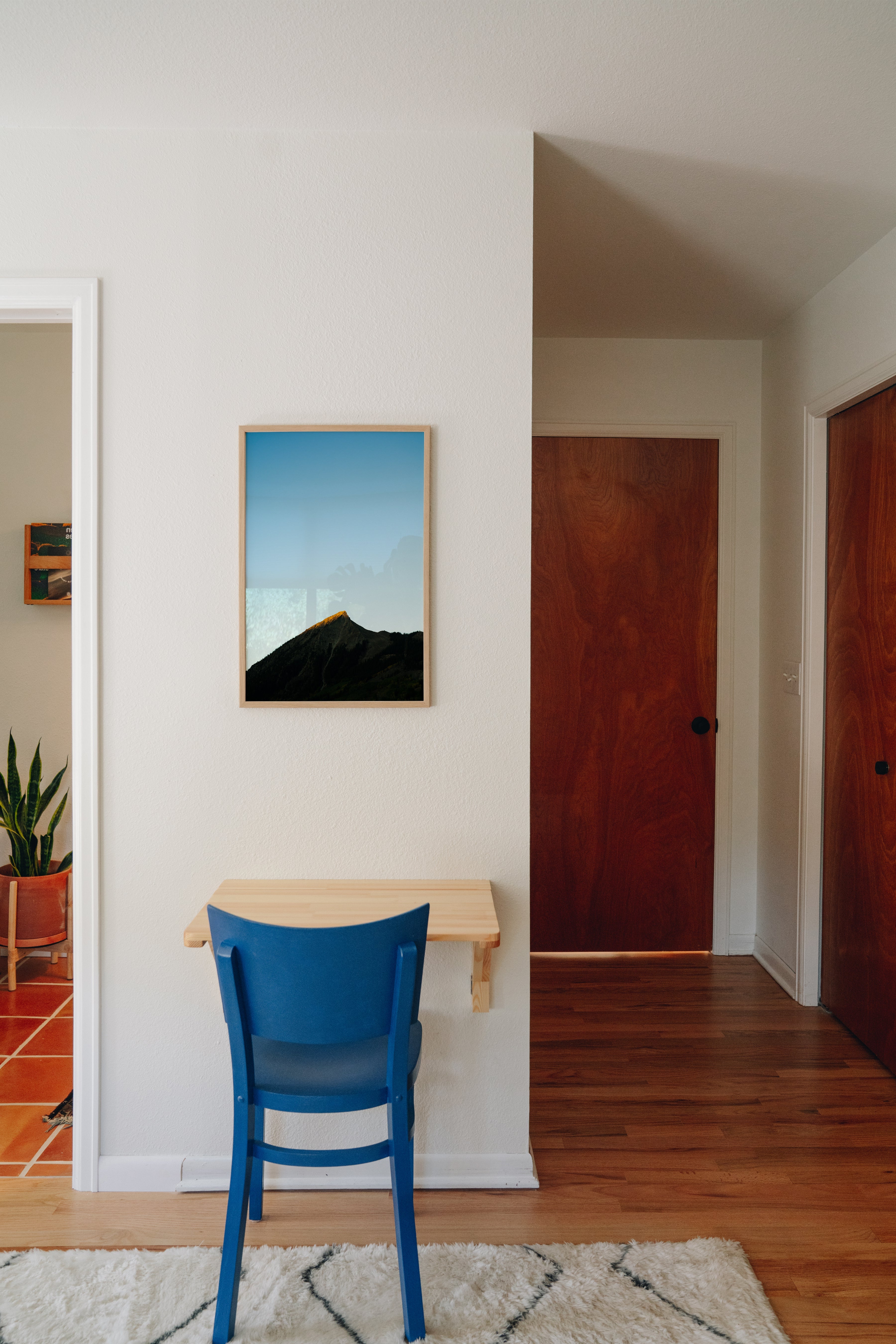 Framed mountain photography artwork on a wall with a blue chair below it.