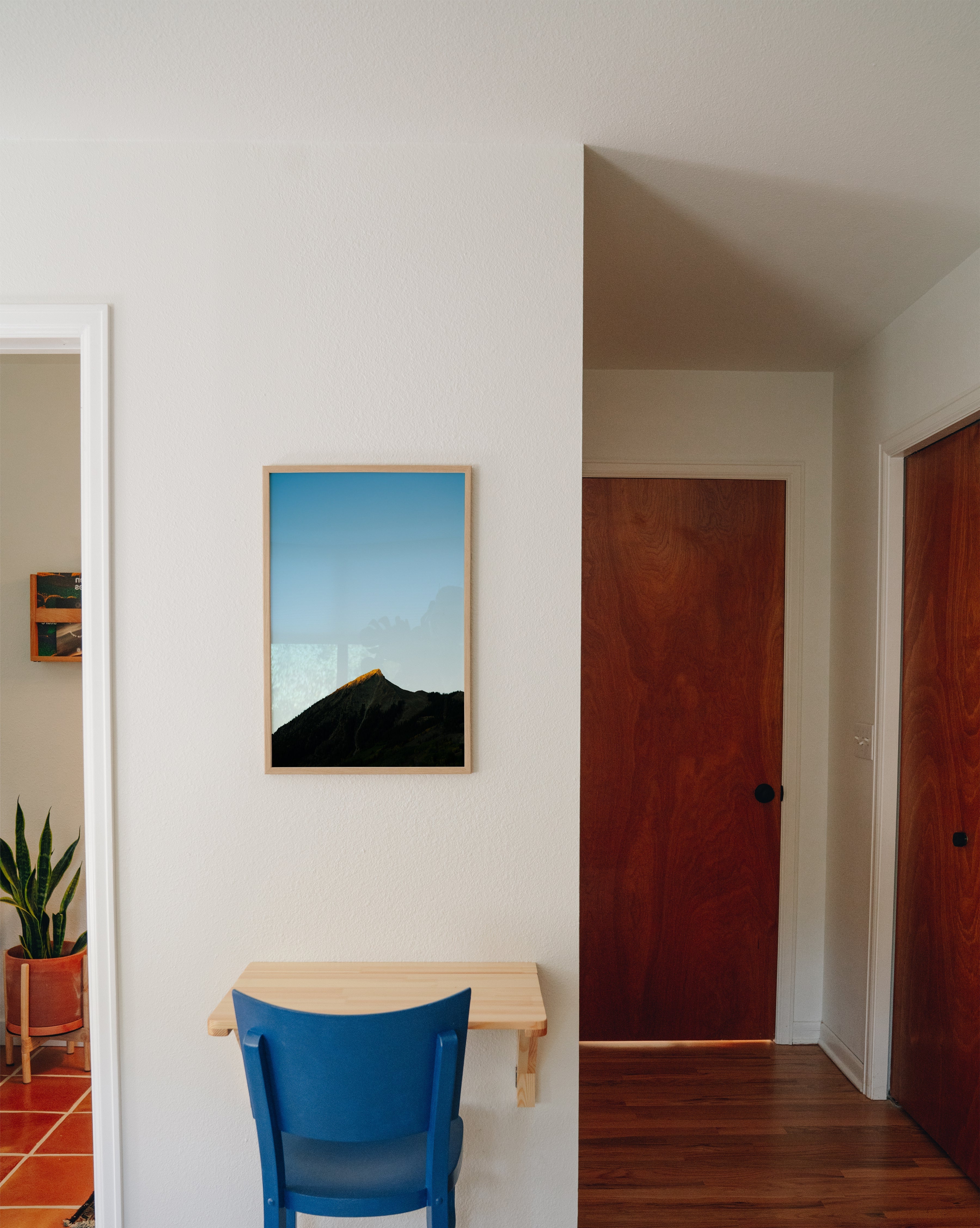 Mountain landscape photography print displayed in modern hallway with blue chair and minimal decor